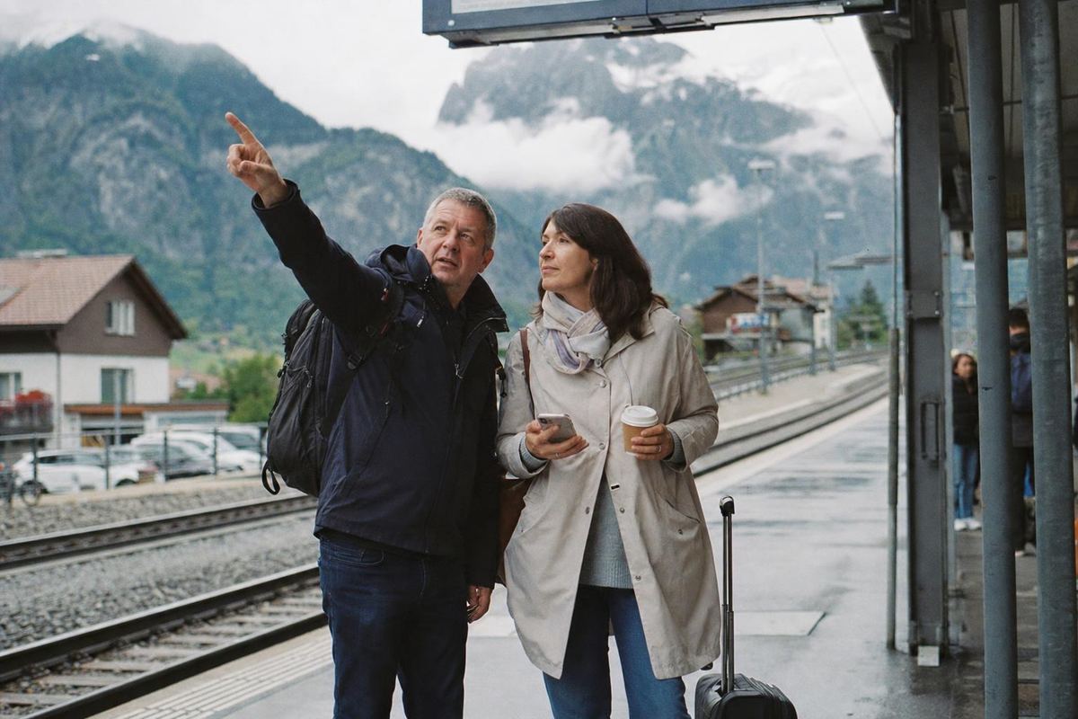 Un couple sur un quai de gare en Suisse, les montagnes derrière eux